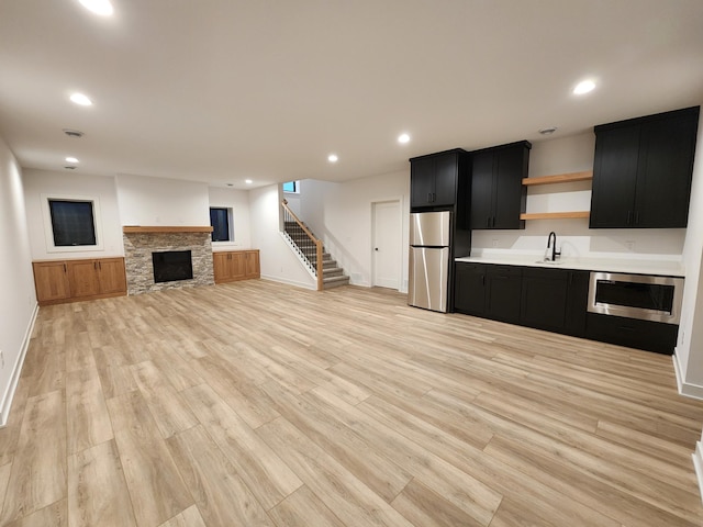 unfurnished living room with recessed lighting, stairway, light wood-style flooring, a sink, and a stone fireplace