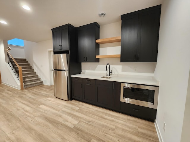 kitchen with open shelves, stainless steel appliances, light wood-style floors, a sink, and dark cabinetry