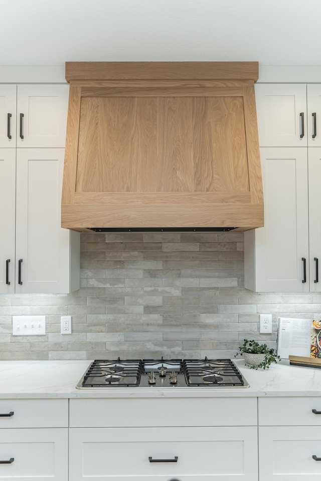 kitchen with stainless steel gas cooktop, wall chimney range hood, and white cabinetry