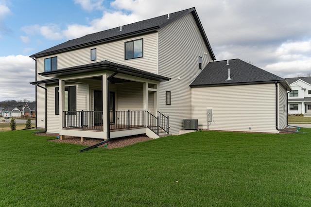 rear view of property featuring central air condition unit, a porch, a lawn, and roof with shingles