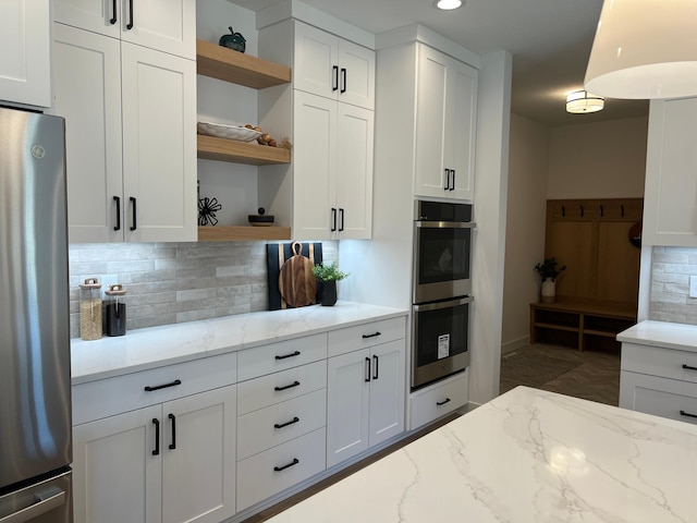 kitchen featuring white cabinets, appliances with stainless steel finishes, light stone countertops, open shelves, and tasteful backsplash