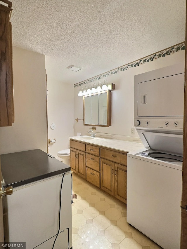 bathroom with vanity, a textured ceiling, stacked washing maching and dryer, and toilet