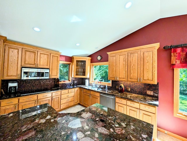 kitchen featuring stainless steel appliances, dark stone countertops, sink, vaulted ceiling, and backsplash