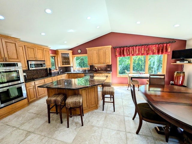 kitchen with lofted ceiling, a kitchen island, stainless steel appliances, a breakfast bar, and backsplash