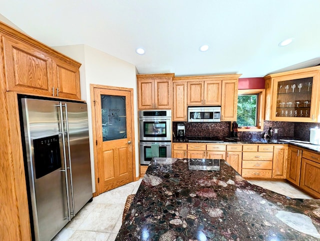 kitchen featuring appliances with stainless steel finishes, backsplash, vaulted ceiling, and dark stone counters