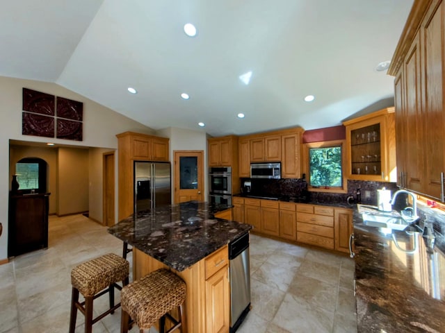 kitchen featuring stainless steel appliances, dark stone countertops, sink, vaulted ceiling, and a kitchen bar