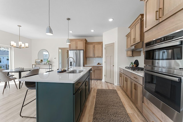 kitchen with light wood-type flooring, stainless steel appliances, sink, decorative light fixtures, and a center island with sink