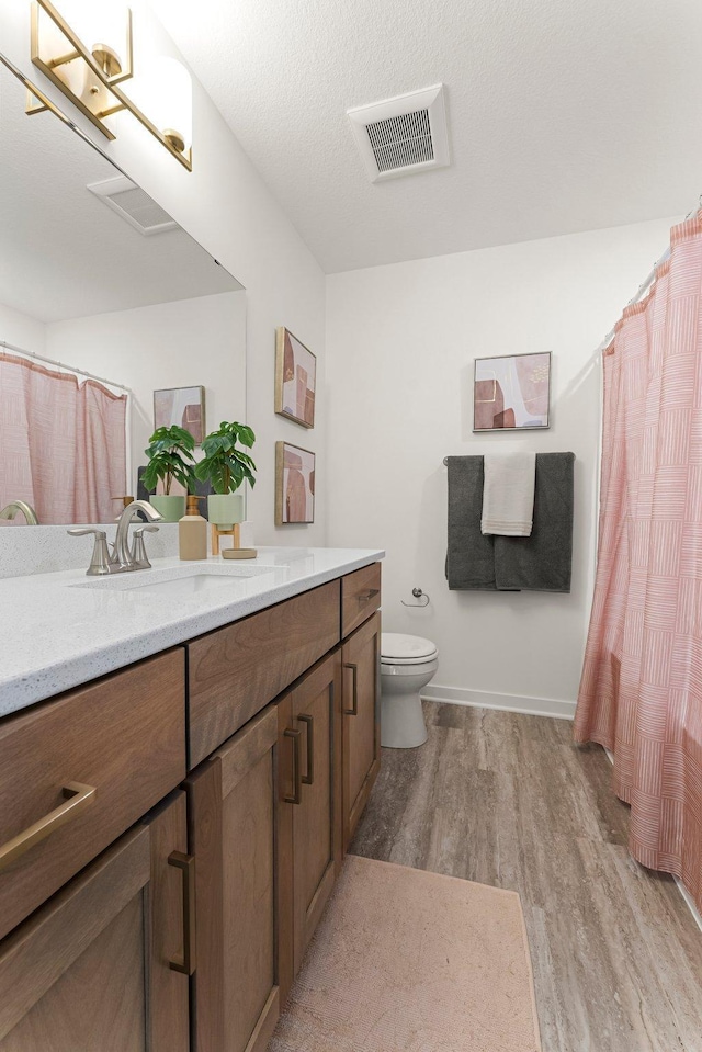 bathroom with hardwood / wood-style floors, vanity, toilet, and a textured ceiling