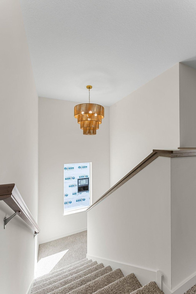 stairs with carpet flooring, a textured ceiling, and a notable chandelier