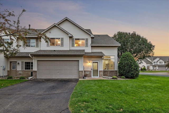 view of front of property featuring an attached garage, a yard, driveway, and a shingled roof