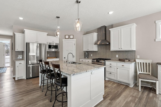 kitchen featuring dark wood-style flooring, a sink, stainless steel appliances, white cabinetry, and wall chimney exhaust hood