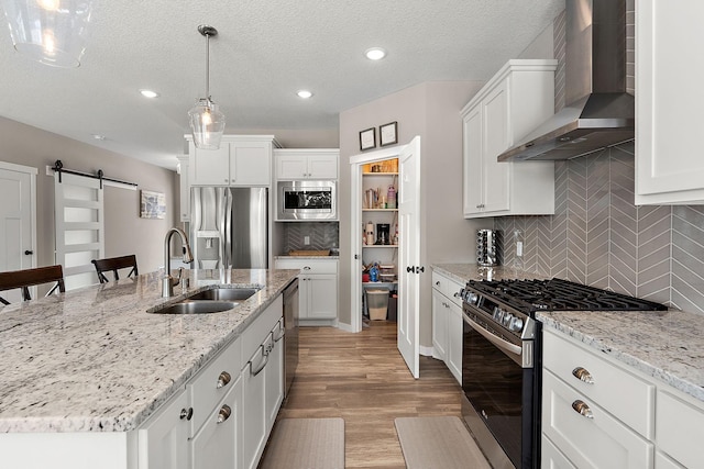 kitchen featuring a sink, a barn door, light wood-style floors, appliances with stainless steel finishes, and wall chimney range hood