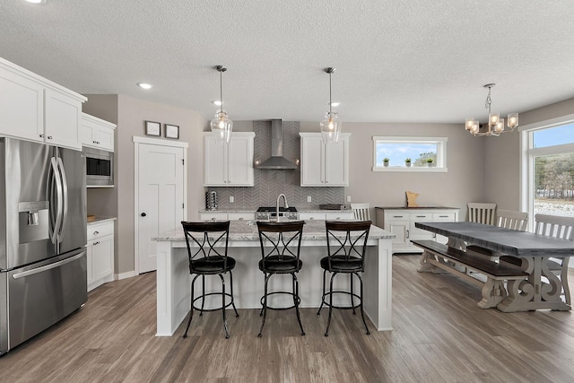 kitchen featuring white cabinets, appliances with stainless steel finishes, wall chimney range hood, and wood finished floors