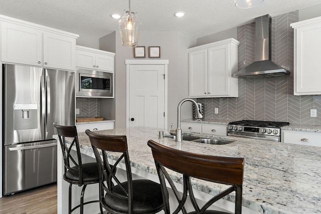 kitchen with white cabinets, appliances with stainless steel finishes, wall chimney range hood, and a sink