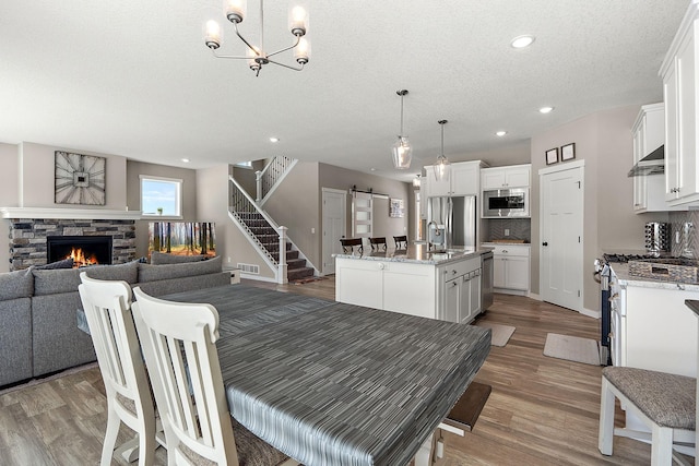 dining area featuring light wood-style flooring, stairs, a stone fireplace, a textured ceiling, and a barn door