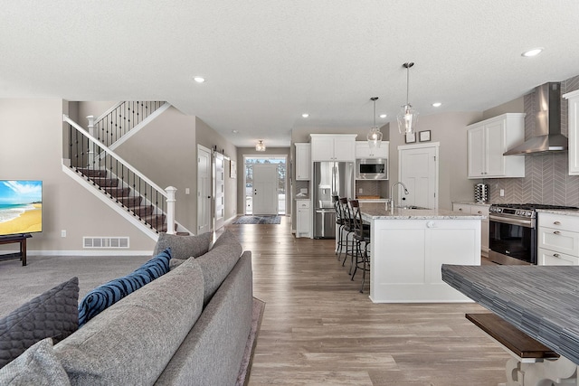 kitchen with visible vents, open floor plan, a barn door, appliances with stainless steel finishes, and wall chimney exhaust hood