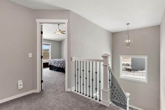 hall with an upstairs landing, a notable chandelier, a textured ceiling, carpet flooring, and baseboards