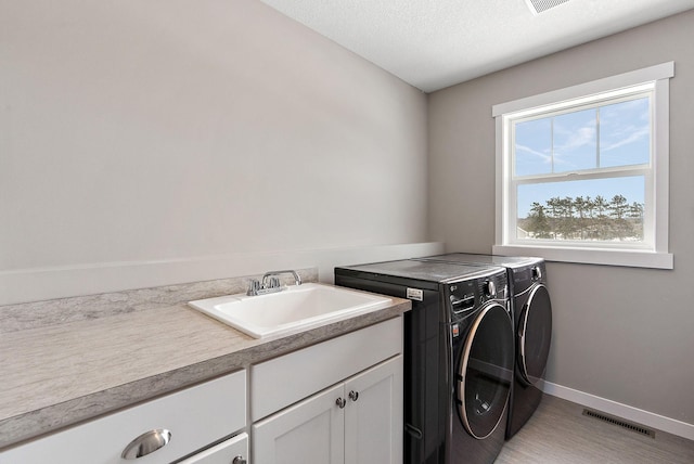 washroom with visible vents, baseboards, washing machine and dryer, cabinet space, and a sink