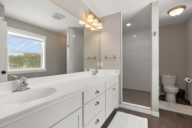 full bathroom featuring visible vents, double vanity, a tile shower, a sink, and toilet