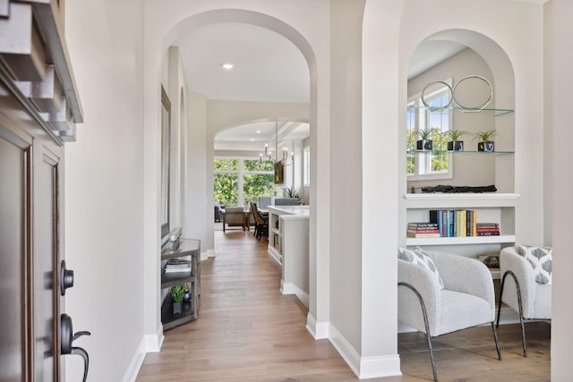 corridor with an inviting chandelier and light hardwood / wood-style flooring