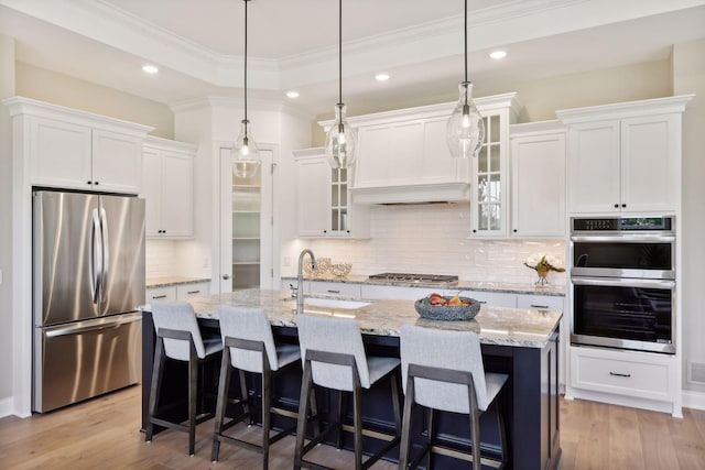 kitchen with light wood-type flooring, stainless steel appliances, white cabinets, and a center island with sink