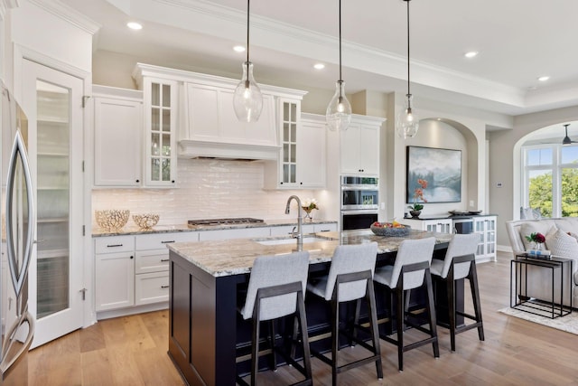 kitchen featuring a kitchen breakfast bar, an island with sink, light stone counters, light wood-type flooring, and white cabinets