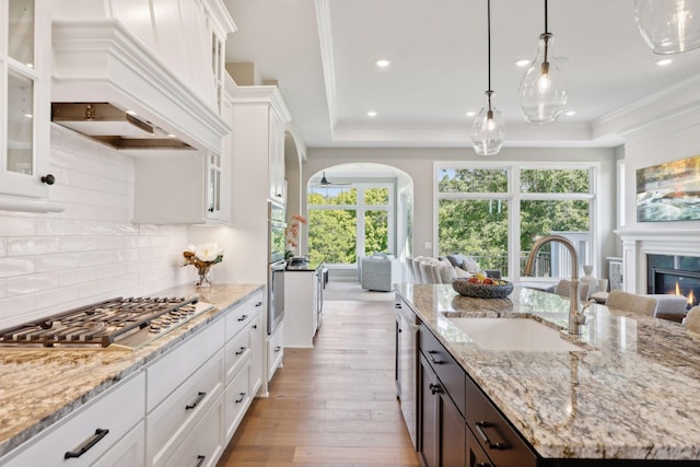 kitchen with white cabinets, light wood-type flooring, custom exhaust hood, sink, and an island with sink