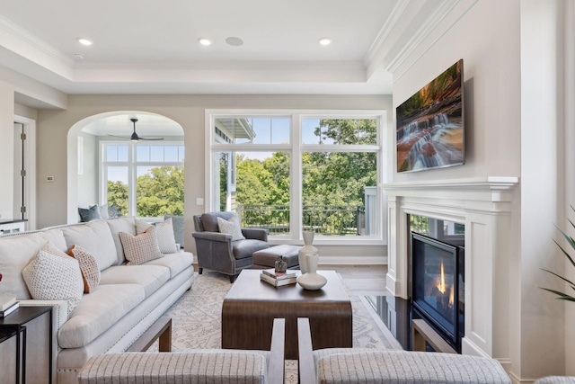 living room featuring light wood-type flooring, a raised ceiling, ornamental molding, and ceiling fan