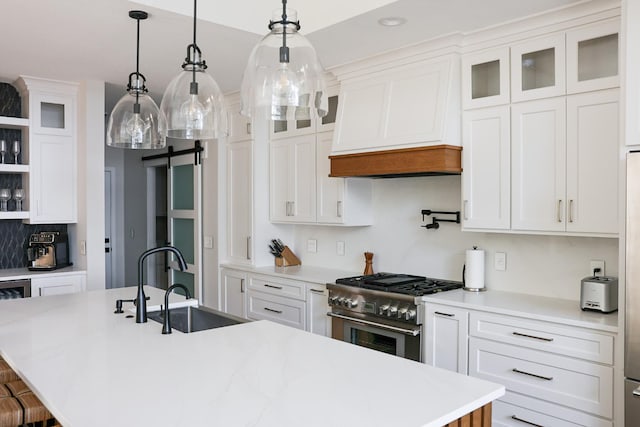 kitchen with an island with sink, pendant lighting, stainless steel range, and white cabinetry