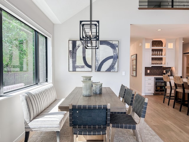 dining space with beverage cooler, lofted ceiling, indoor bar, and light hardwood / wood-style flooring