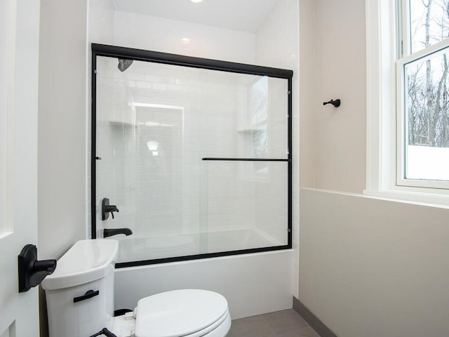 bathroom with combined bath / shower with glass door, toilet, and a healthy amount of sunlight