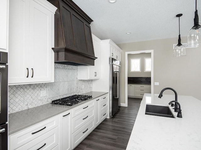 kitchen featuring sink, hanging light fixtures, stainless steel appliances, custom range hood, and white cabinets