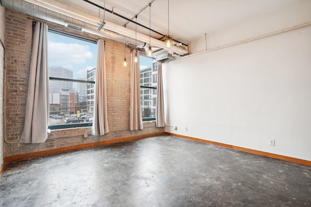 spare room featuring a wealth of natural light, concrete floors, and brick wall