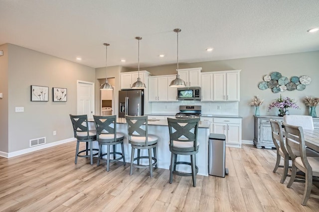 kitchen featuring light wood-type flooring, white cabinetry, a kitchen bar, hanging light fixtures, and appliances with stainless steel finishes