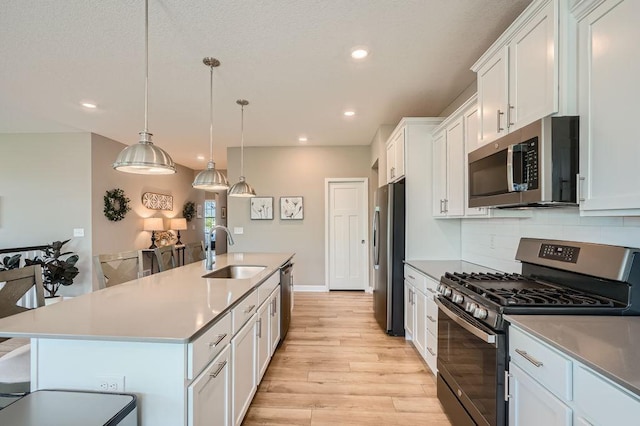 kitchen featuring a kitchen island with sink, sink, appliances with stainless steel finishes, white cabinets, and light hardwood / wood-style floors