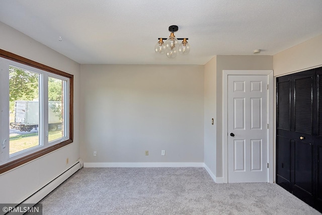 empty room featuring a textured ceiling, a chandelier, light colored carpet, and a baseboard radiator