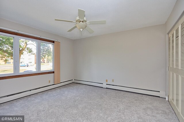 unfurnished bedroom featuring a baseboard heating unit, light carpet, ceiling fan, and a closet