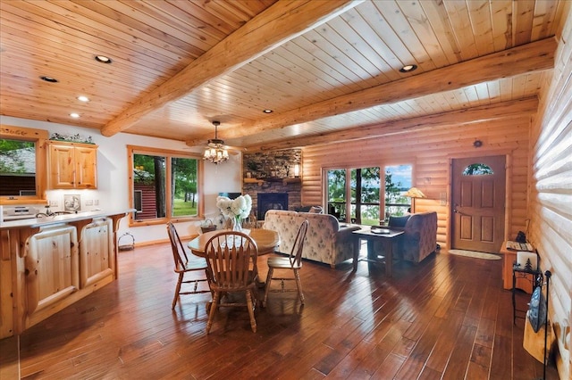 dining area featuring beam ceiling, rustic walls, a stone fireplace, a healthy amount of sunlight, and dark wood-style flooring