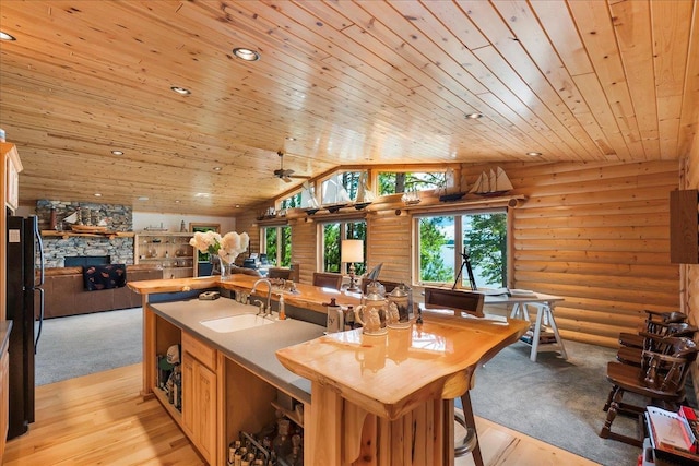 kitchen with a sink, rustic walls, a stone fireplace, wood ceiling, and vaulted ceiling