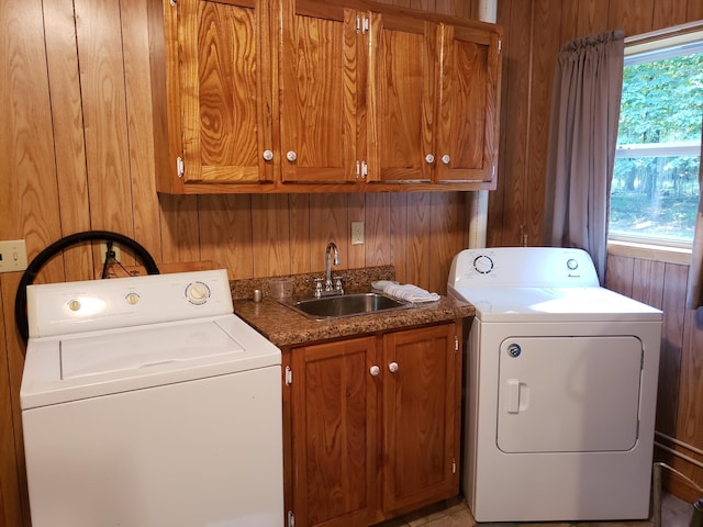 washroom with cabinets, wood walls, washer and clothes dryer, and sink