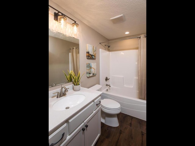 full bathroom with toilet, hardwood / wood-style floors, vanity, a textured ceiling, and shower / tub combo