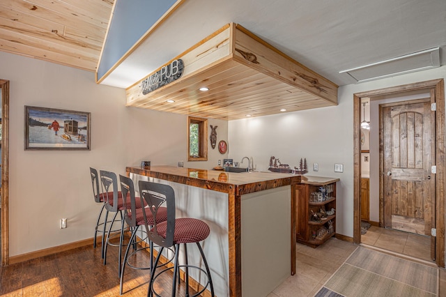 kitchen featuring wood ceiling, hardwood / wood-style flooring, kitchen peninsula, butcher block counters, and a kitchen breakfast bar