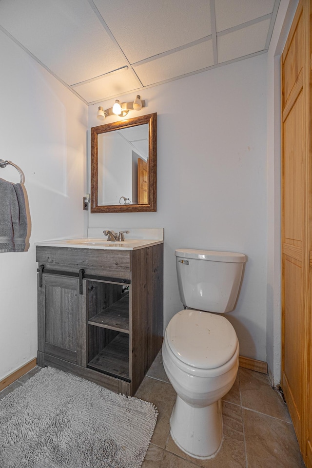 bathroom featuring vanity, a drop ceiling, toilet, and tile patterned floors