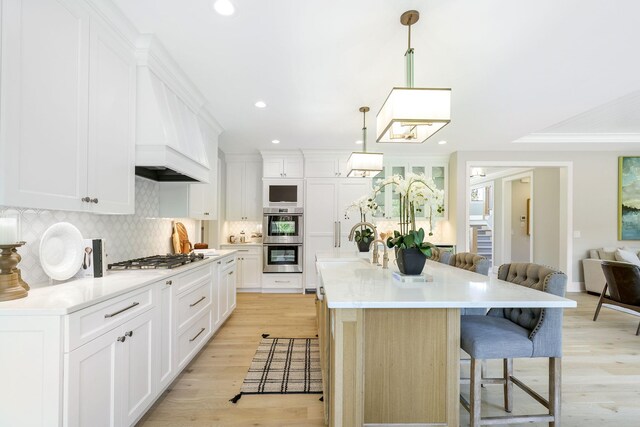 kitchen with decorative light fixtures, stainless steel appliances, light hardwood / wood-style floors, a kitchen breakfast bar, and a kitchen island with sink