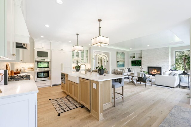 kitchen with a fireplace, an island with sink, light stone countertops, sink, and light hardwood / wood-style floors