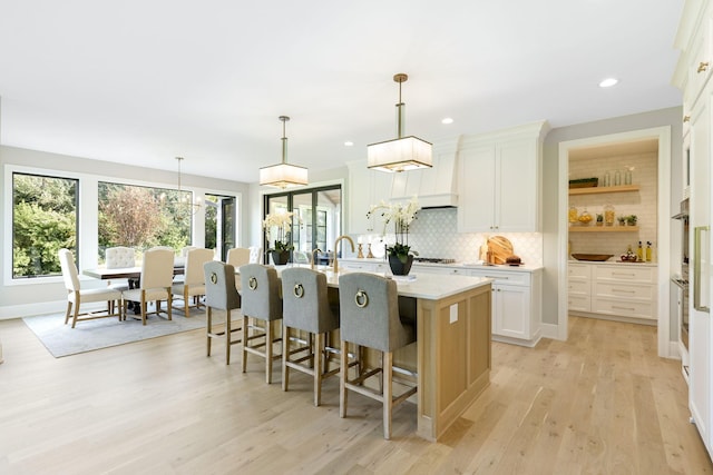 kitchen featuring a center island with sink, light hardwood / wood-style flooring, decorative light fixtures, and white cabinetry