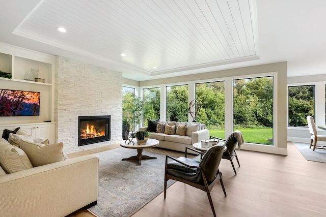 living room with a fireplace, wooden ceiling, light hardwood / wood-style floors, a tray ceiling, and built in features