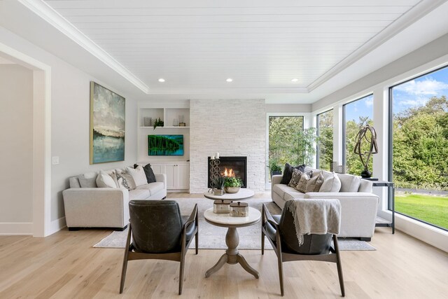 living room with built in features, ornamental molding, a stone fireplace, and light wood finished floors
