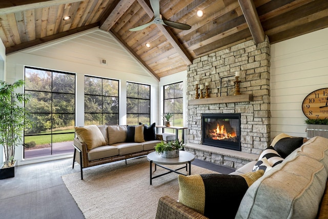 living room with wood ceiling, plenty of natural light, beam ceiling, and a stone fireplace