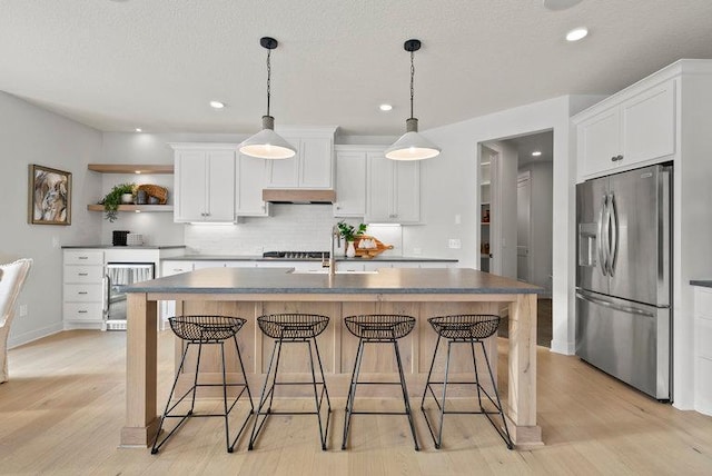 kitchen with white cabinets, light hardwood / wood-style flooring, an island with sink, stainless steel refrigerator with ice dispenser, and a breakfast bar